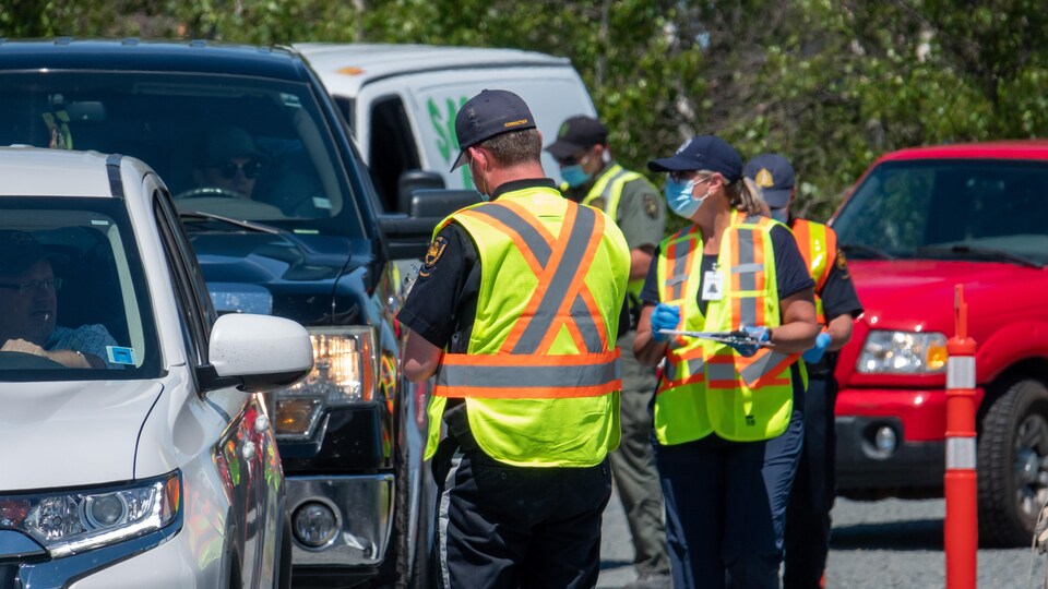 Un agent debout, de dos et portant une veste jaune, parle à un automobiliste qui est dans sa voiture.