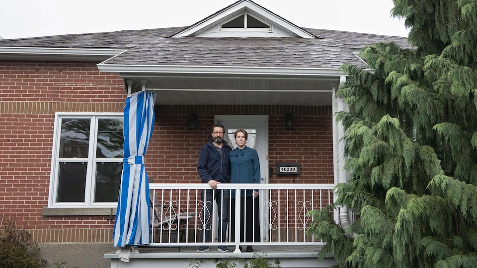 Un couple debout sur le balcon de sa maison.