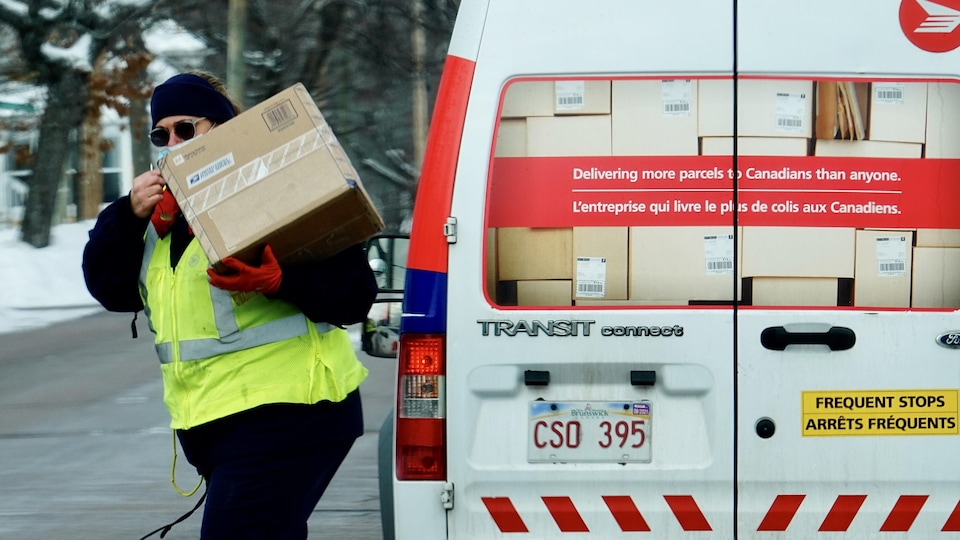 Une travailleuse de Postes Canada s'éloigne de son camion avec un colis, le 14 janvier 2021 au Nouveau-Brunswick.