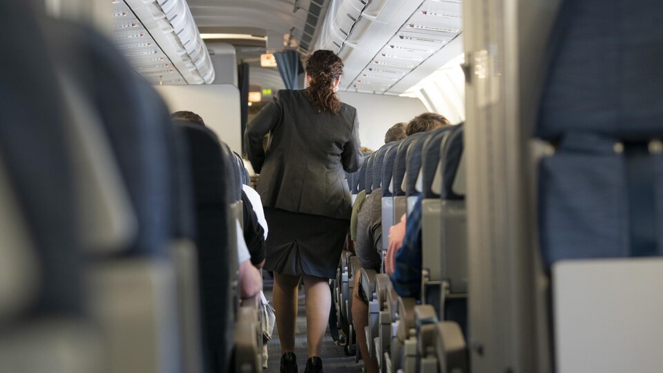 Une agente de bord marche au milieu d'une rangée à bord d'un avion.