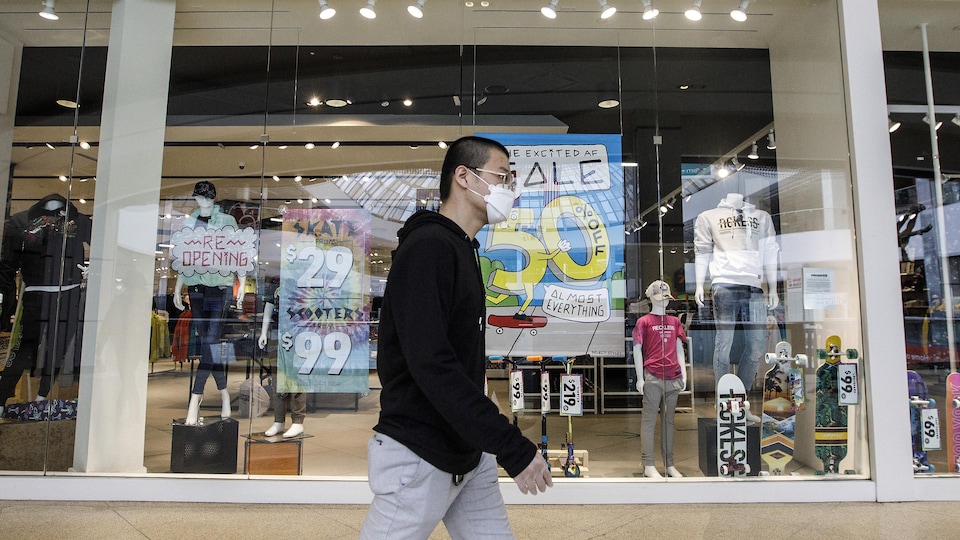 Un homme marche devant un magasin avec un masque.