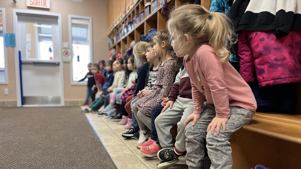 Des enfants sont assis en rang, le visage tourné vers la porte de la garderie.