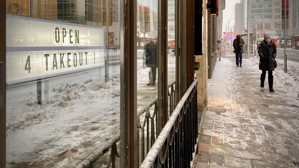 Des piétons marchent près d'une affiche sur laquelle il est écrit « ouvert, pour emporter ».