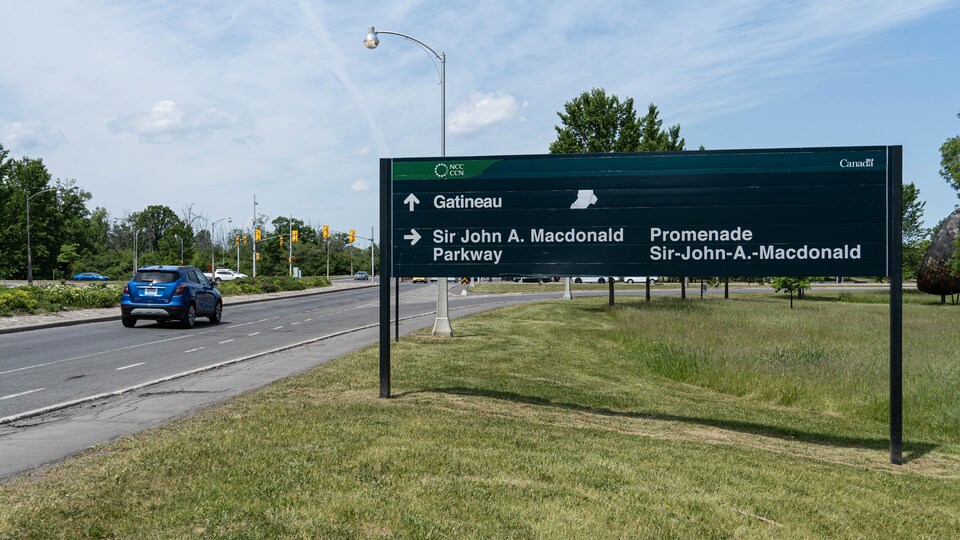 Un panneau indiquant la Promenade Sir-John-A.-Macdonald avec une voiture qui roule en fond.