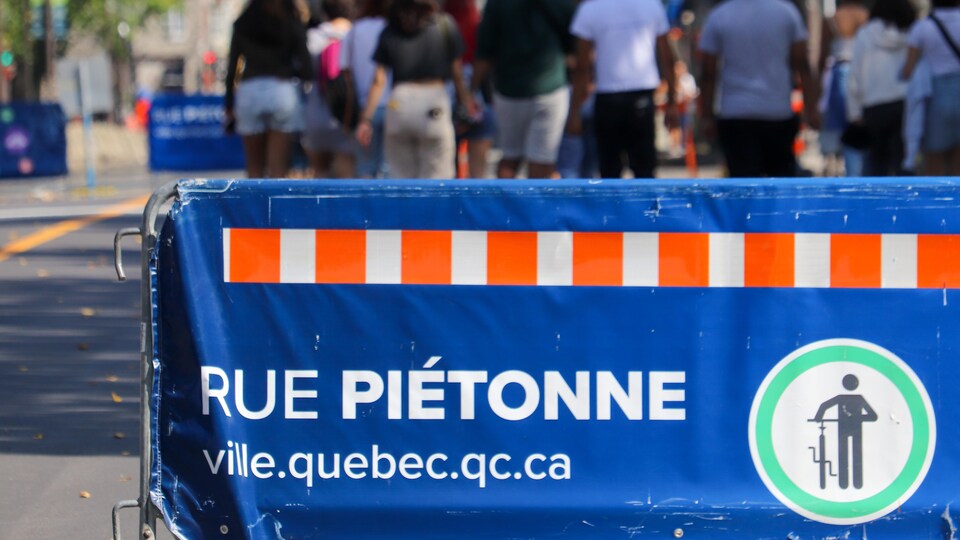 Des gens circulent à pied sur une portion piétonnière de la Grande Allée en été. À l'avant-plan, une barrière sur laquelle il est écrit « rue piétonne ».