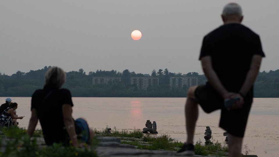 Des personnes regardent le coucher de soleil près de la rivière des Outaouais.