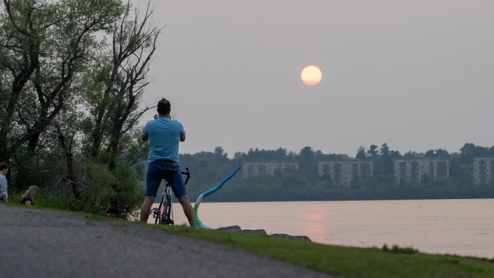 Un cycliste regarde le coucher de soleil près de la rivière des Outaouais.