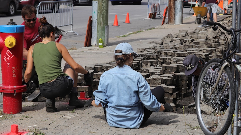 Deux citoyens enlèvent des pavés de béton sur la rue du Roi près d'une borne-fontaine.