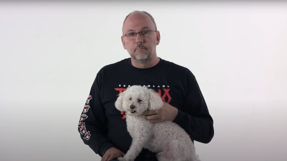Le père, dans un studio blanc, avec un chien sur ses genoux.