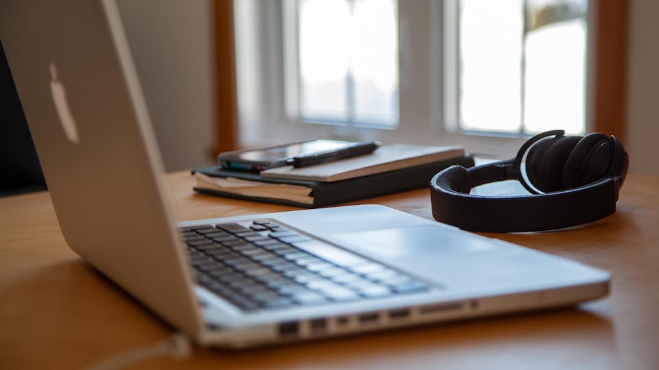 Un ordinateur portable, un casque d'écoute, un agenda, un calepin de notes, un téléphone cellulaire et un stylo posés sur une table, à l'intérieur d'une résidence