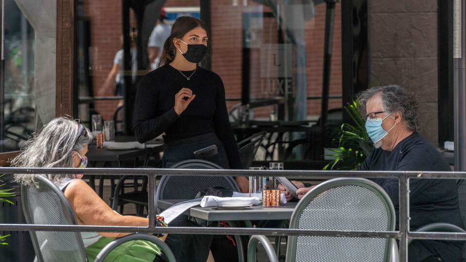 Une serveuse portant le masque parle à deux clients.
