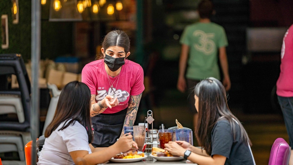 Une serveuse portant le masque discute avec deux clientes.