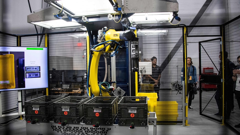 Un grand bras robotisé jaune devant des caisses, dans un entrepôt.