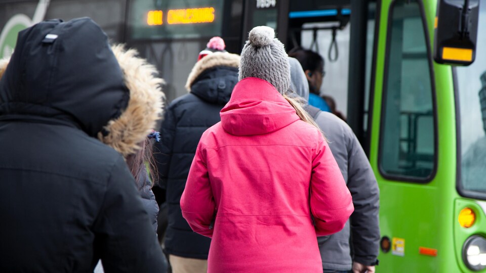Des personnes qui portent des manteaux d'hiver font la file pour monter dans un autobus.