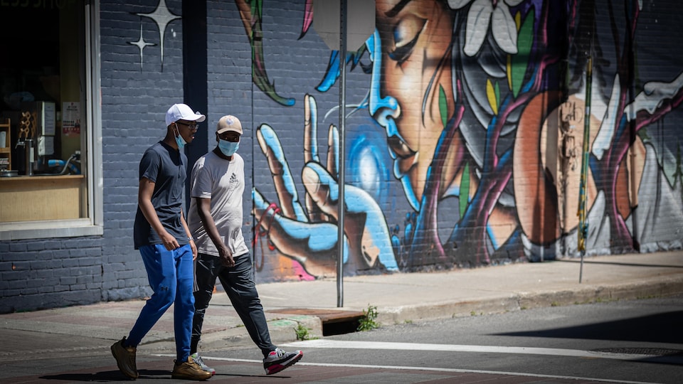 Deux hommes portant le masque traversent une intersection.
