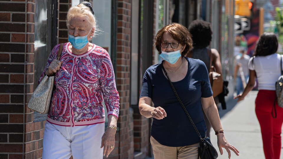 Deux femmes portant le masque marchent sur le trottoir.