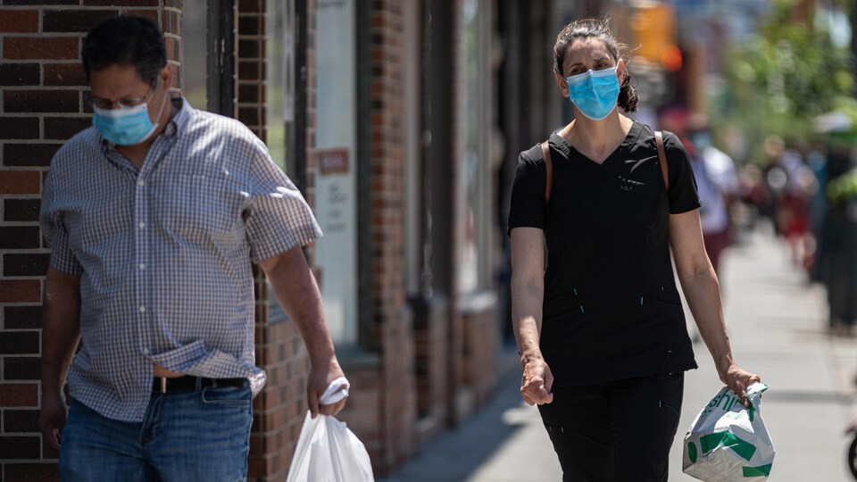 Un homme et une femme portant le masque marchent sur le trottoir.