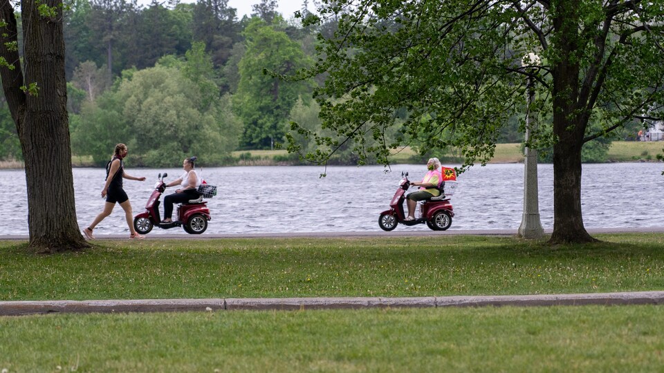 Un piéton et deux personnes en scooter portant un masque au bord d'un lac.