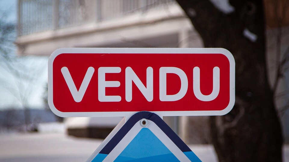 Carton « vendu » installé sur une affiche de courtier immobilier.