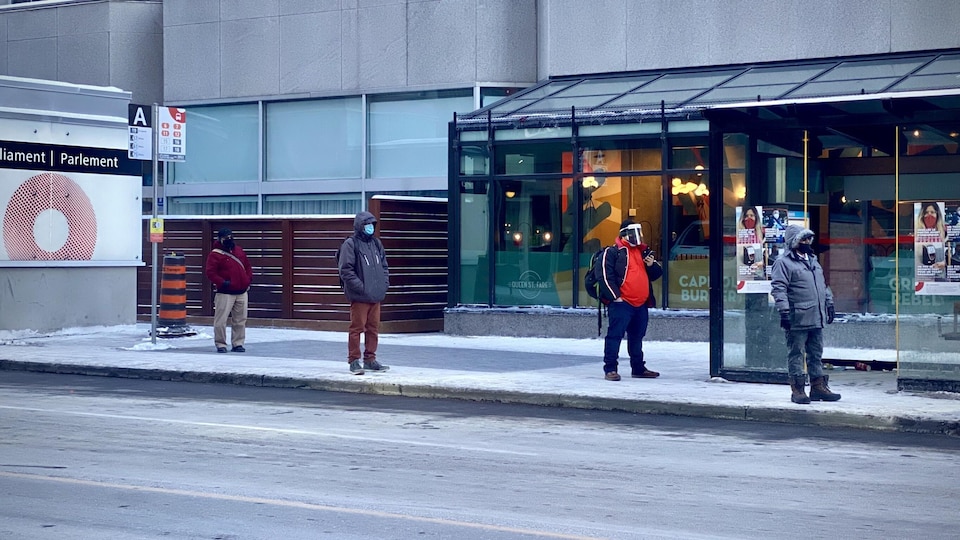 Des personnes attendent l'autobus en maintenant la distanciation physique et en portant le masque.