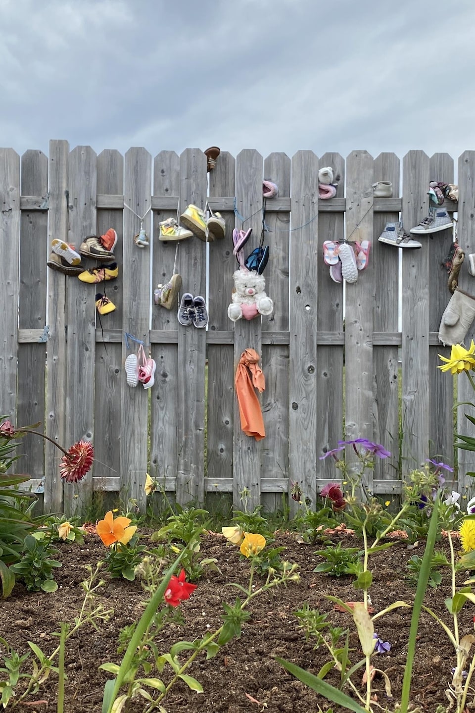 Des fleurs et une clotûre remplie de chaussures d'enfants. 