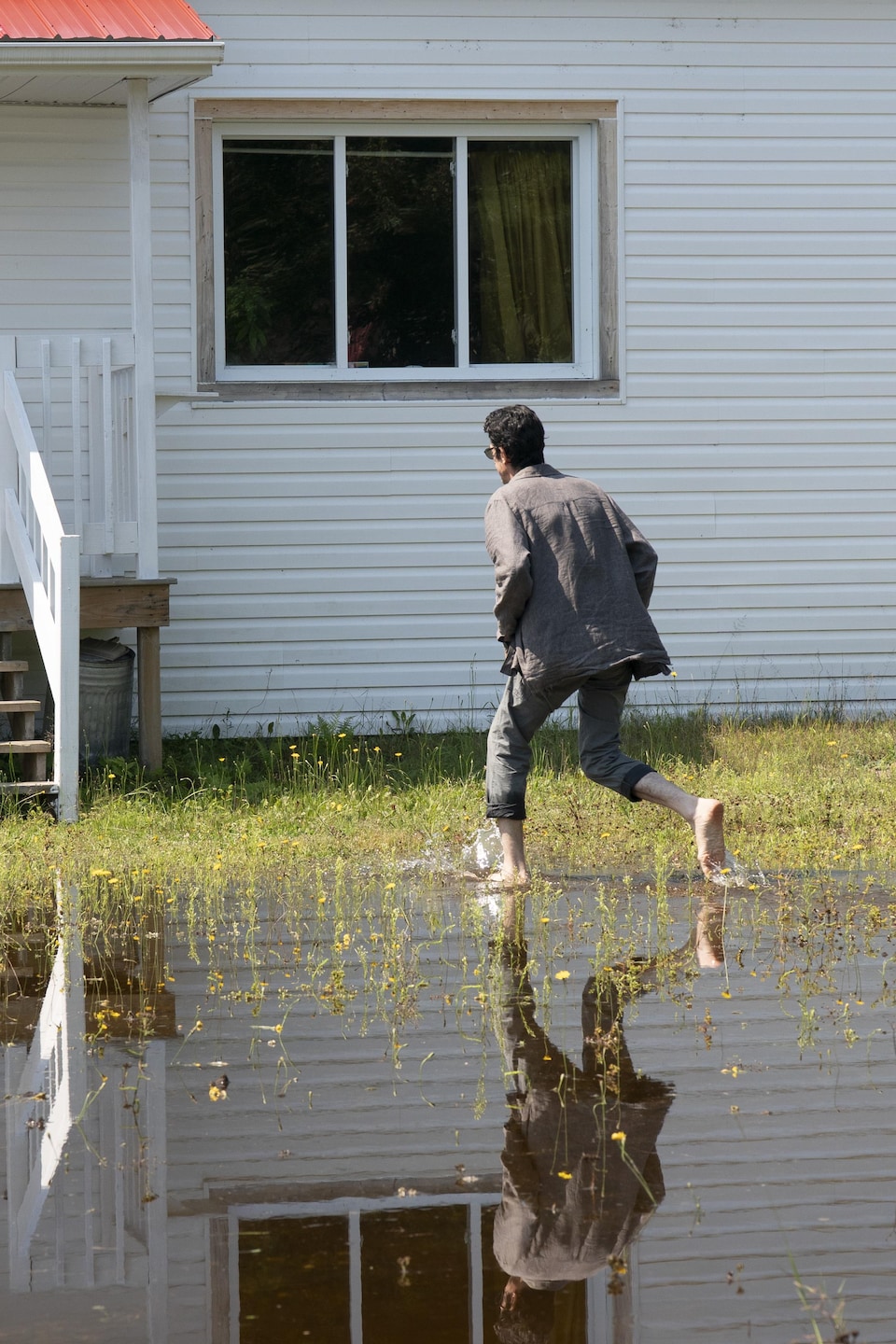 Un homme pieds nus courre vers sa maison sur un terrain inondé.