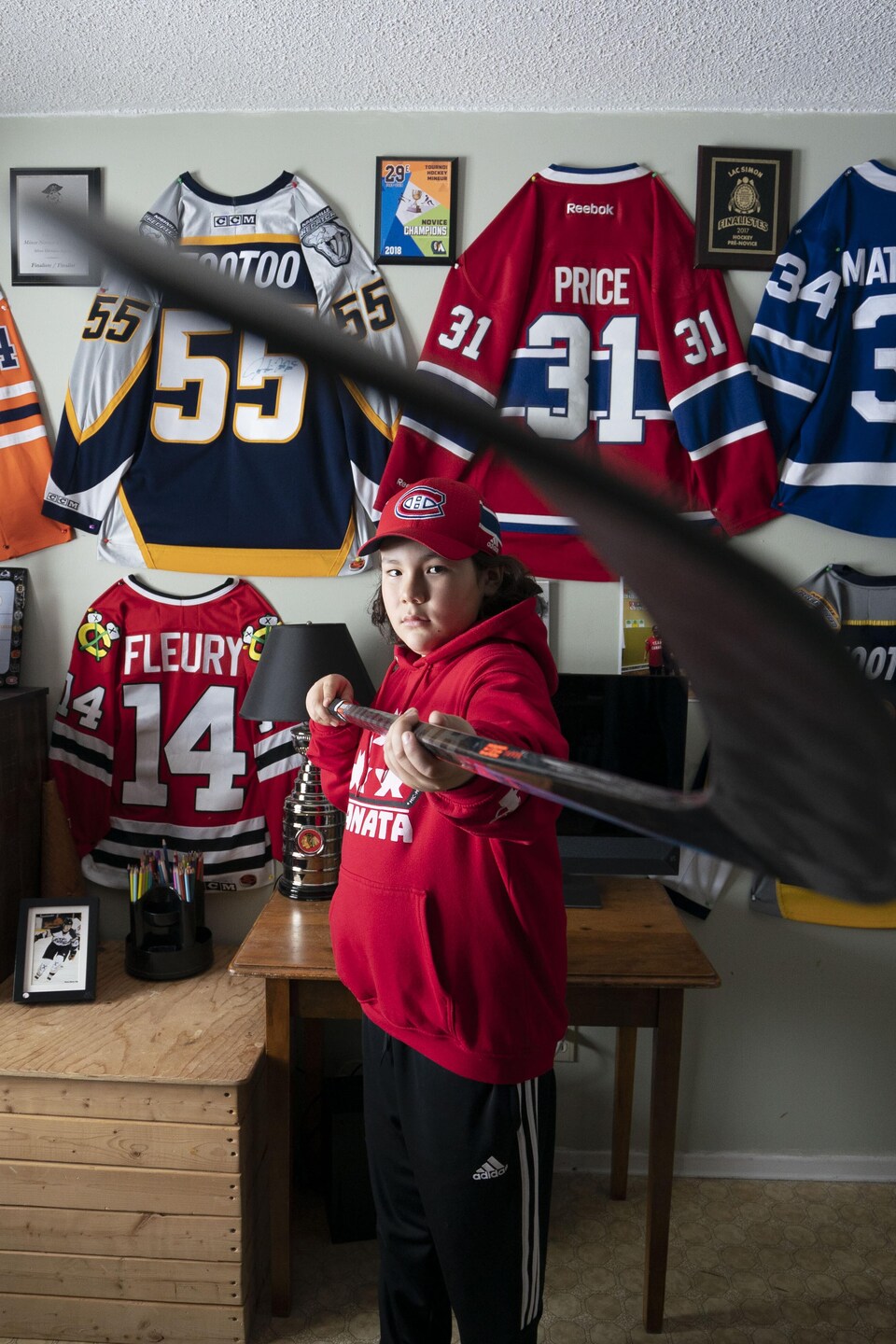 Un enfant dans sa chambre décorée de plusieurs chandails de hockey.