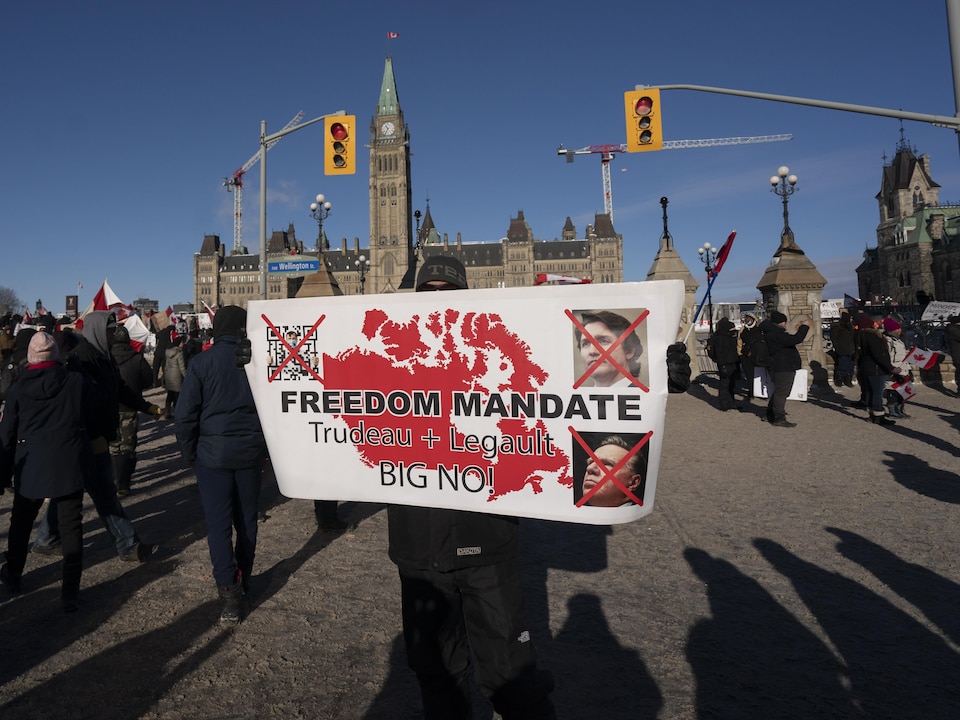 Des gens tiennent une affiche sur laquelle les visages de Justin Trudeau et François Legault sont barrés.