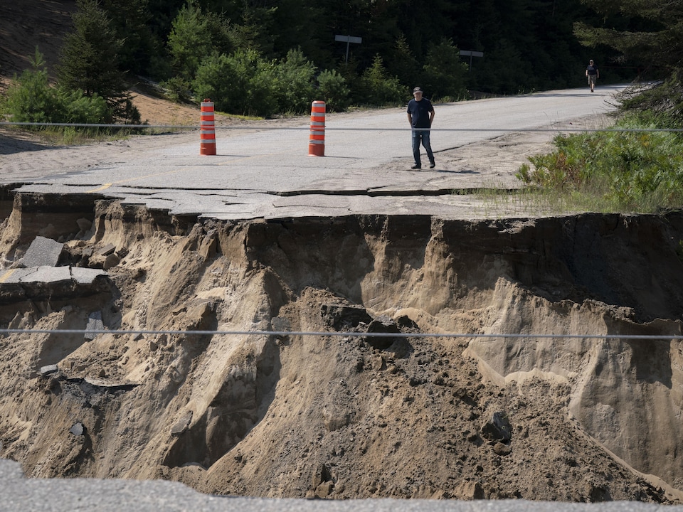 Un homme marche vers le bord d'une grosse crevasse au beau milieu d'une route. 