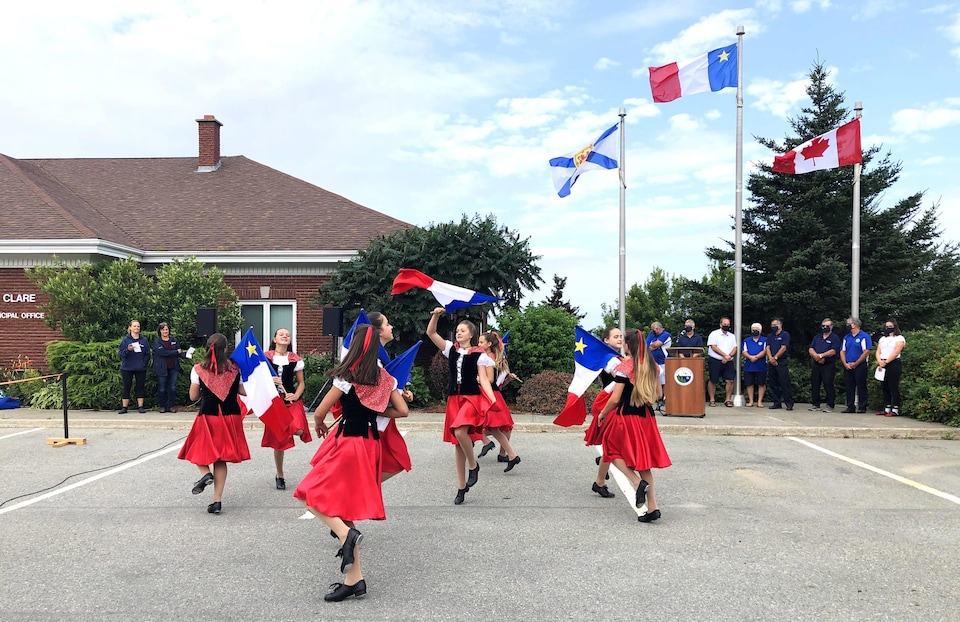 Des jeunes à l'extérieur dansent et agitent des drapeaux de l'Acadie.