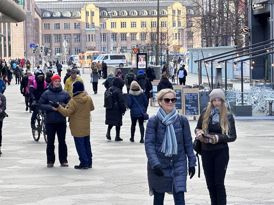 Des Finlandais marchent dans un grande place publique à Helsinki.