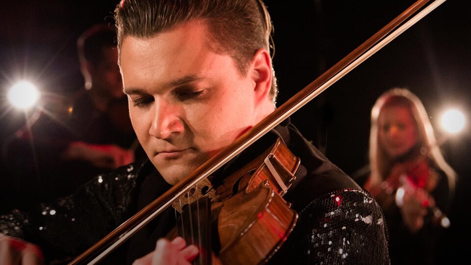 Gros plan sur le visage du jeune homme, qui joue du violon.