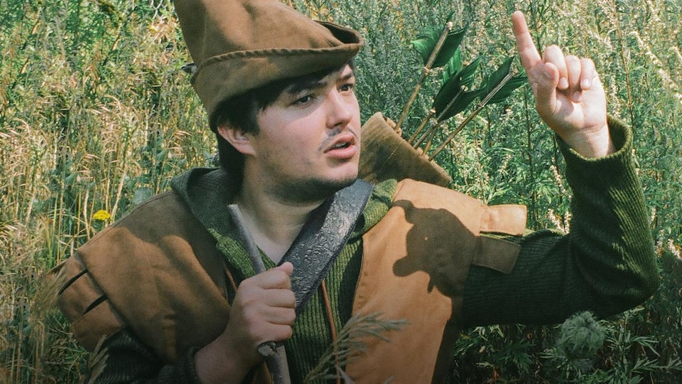 Émilie Bilodeau, à l'extérieur, dans des herbes hautes, vêtu d'un costume de Robin des bois.