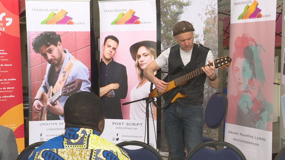 Un musicien joue de la guitare devant des affiches de l'organisme FrancoMusik.