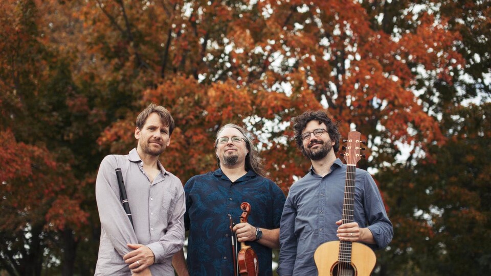 Les trois membres du groupe tenant des instruments photographiés devant un arbre en couleurs