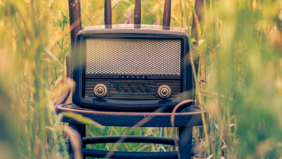 Un poste de radio vintage sur une chaise en bois trônant au milieu d'un champs.