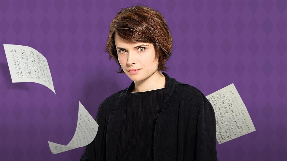 L'artiste pose sur un fond mauve avec ses partitions.