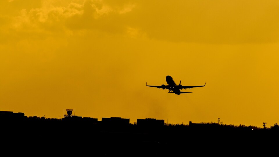Coucher de soleil. Dans un ciel rendu jaune par le coucher du soleil, on distingue la silhouette d'un avion qui décolle.