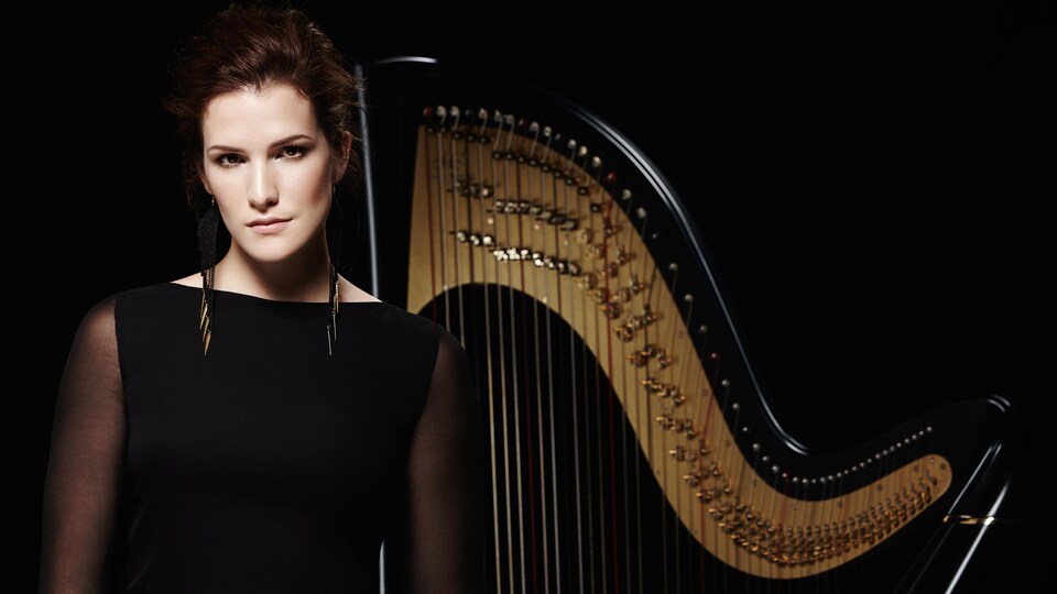 Une musicienne habillée en noir devant une harpe. 