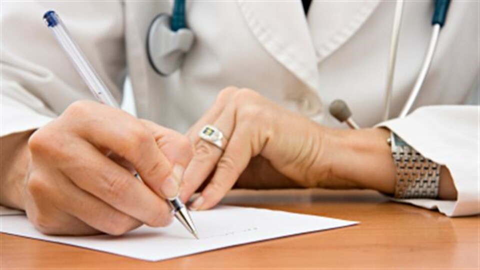 Plan serré des deux mains d'une personne en sarrau écrivant une ordonnance.