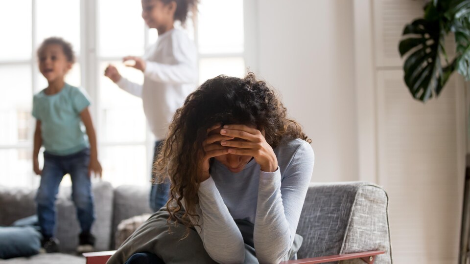 Une femme se prend la tête pendant que ses deux jeunes enfants sautent derrière.