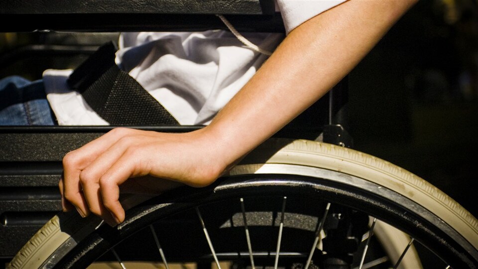 Plan serré d'une main manoeuvrant la roue d'un fauteuil roulant.