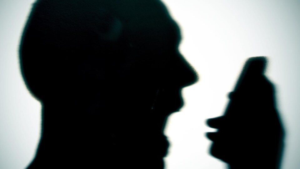 La silhouette d'un homme qui crie vers un téléphone dans sa main.