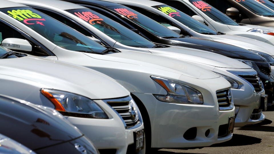 Plusieurs voitures sont stationnées dans une concession automobile avec des prix de vente affichés sur leur pare-brise.