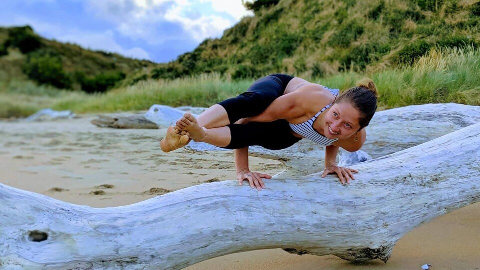 Andréann Duquet, faisant de l'acro-yoga sur un tronc d'arbre, sur une plage