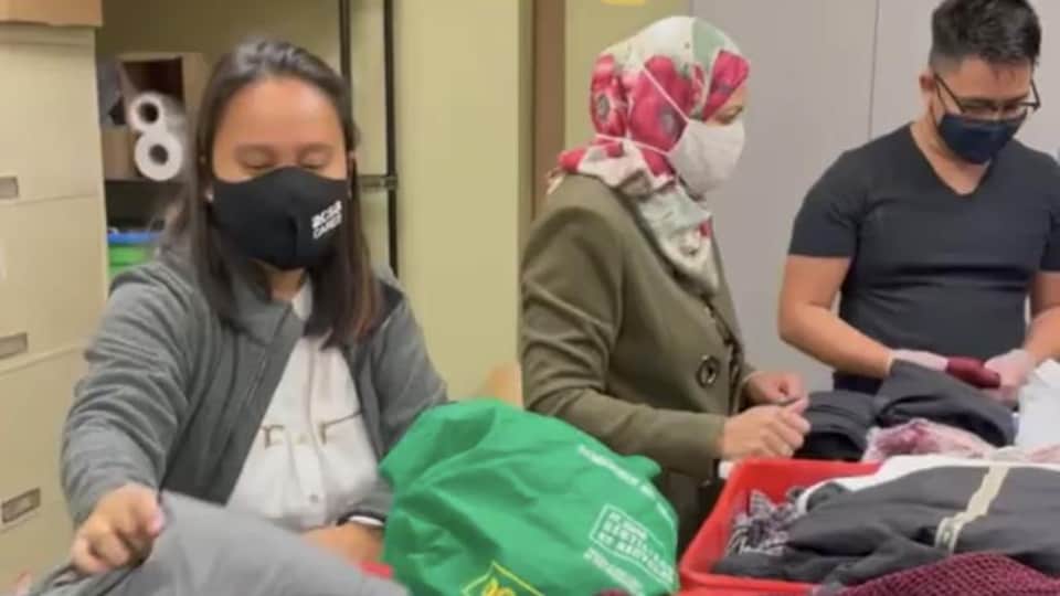 Deux femmes et un homme trient des sacs de vêtements dans les locaux d'un organisme de charité. 
