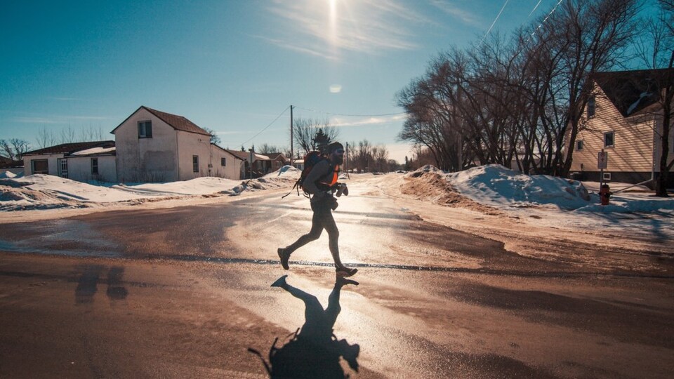 Un athlète barbu porte un sac à dos en courant dans la rue en plein hiver.