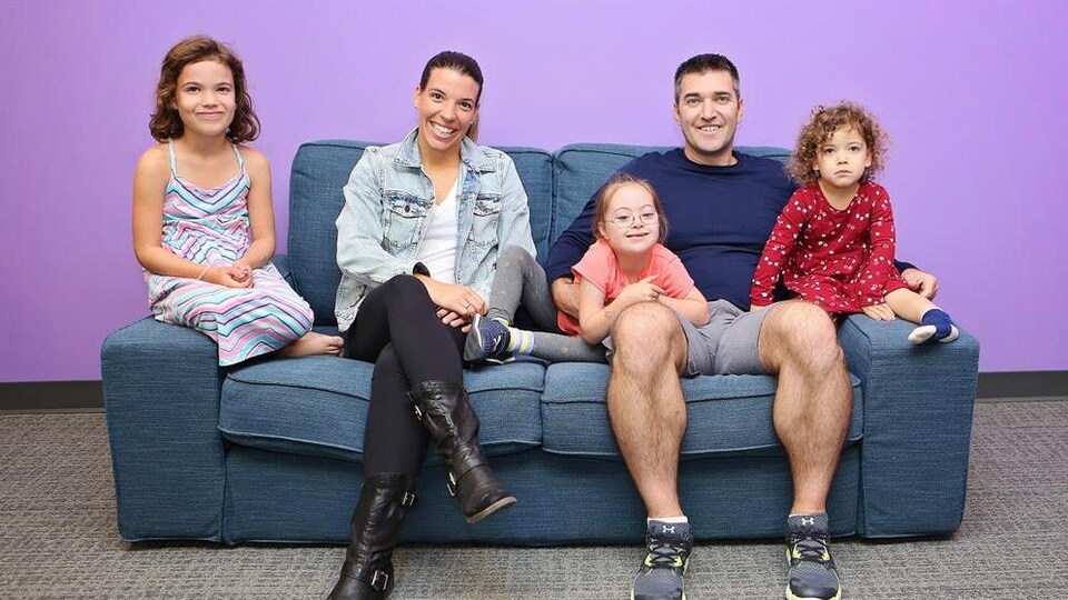 Deux parents et leurs trois fillettes assis sur un fauteuil sourient à la caméra.