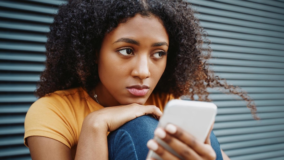 Une adolescente regarde au loin en tenant un téléphone intelligent dans sa main. 