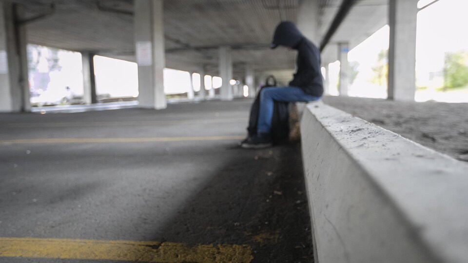  Un jeune adolescent assis, la tête baissée, dans un stationnement.